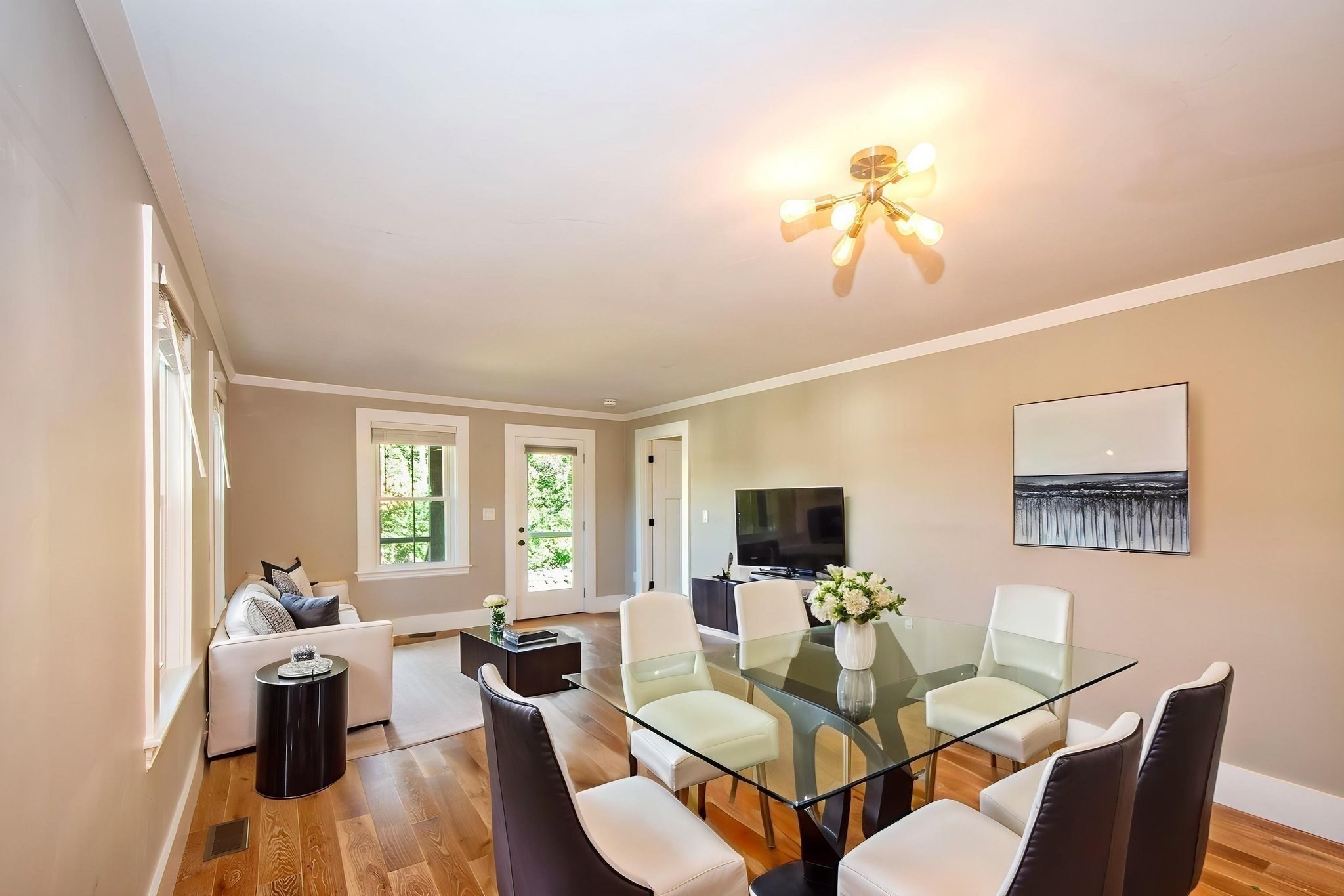 Living and dining area with a glass table, white chairs, hardwood floors, and a window-side sofa.