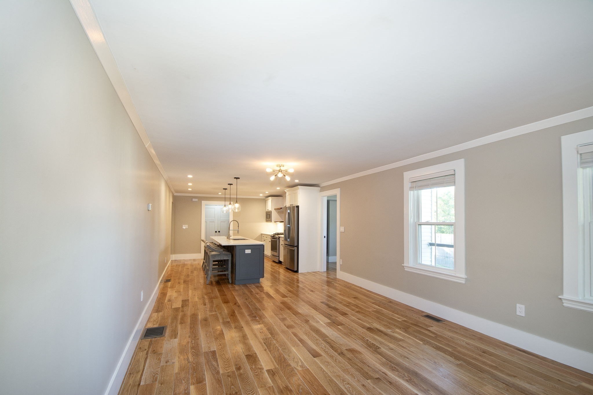 Open-plan kitchen with blue-gray island, bar stools, stainless steel appliances, and warm wood floors.