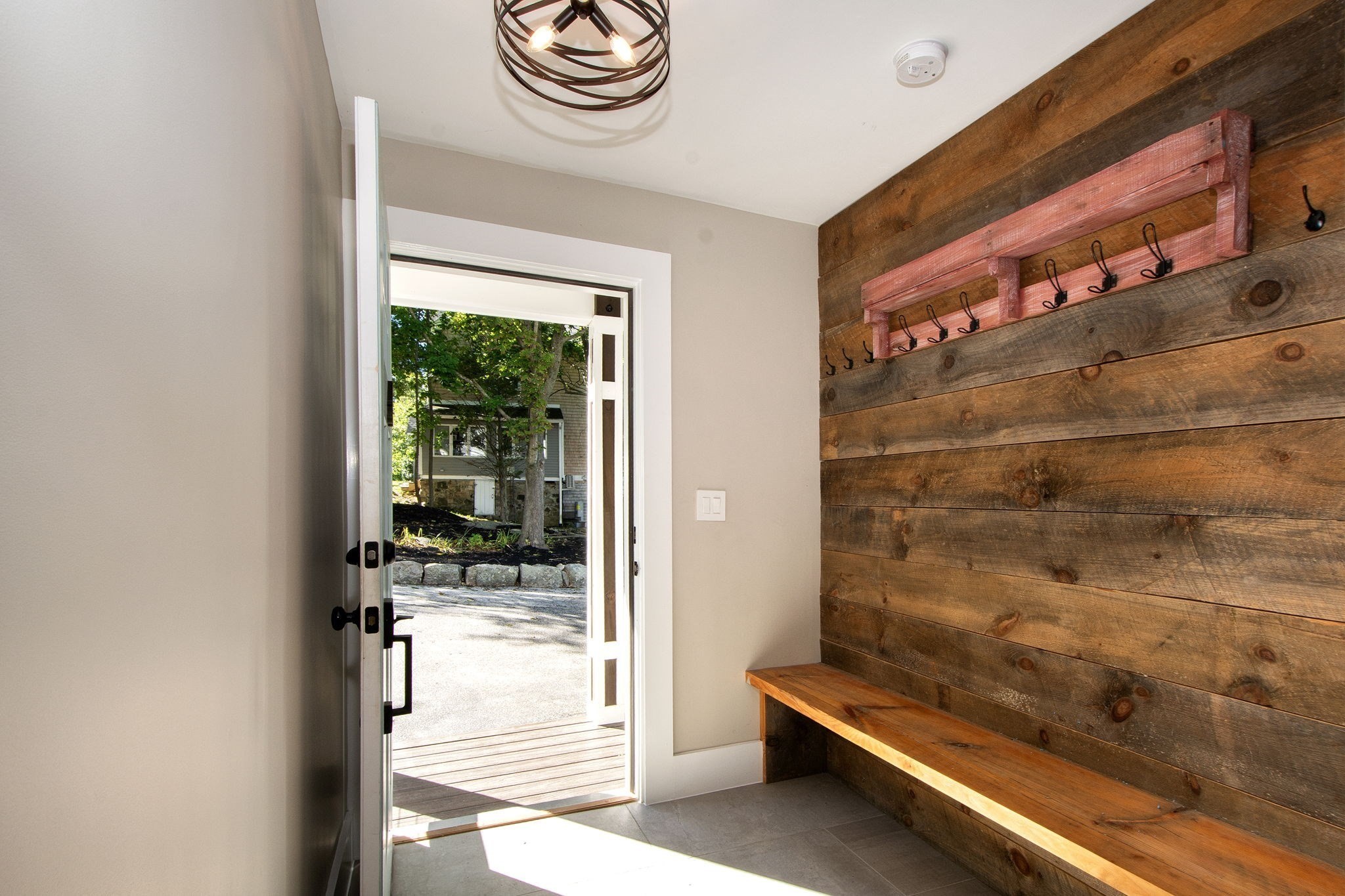 Entryway with a long wooden bench, rustic coat-hook wall, and open glass door.