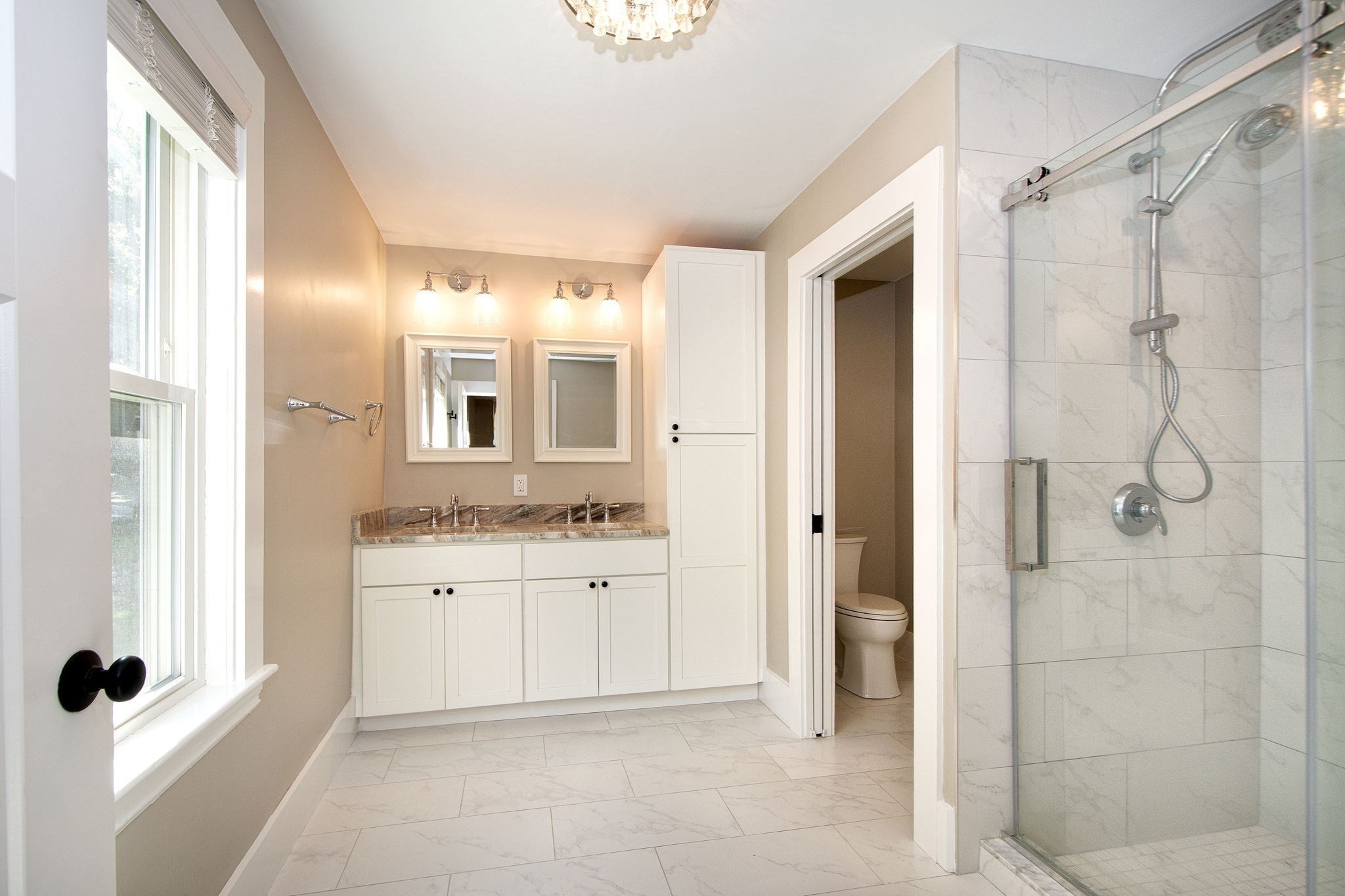 Bright bathroom with a double vanity, glass-enclosed tiled shower, and large window.