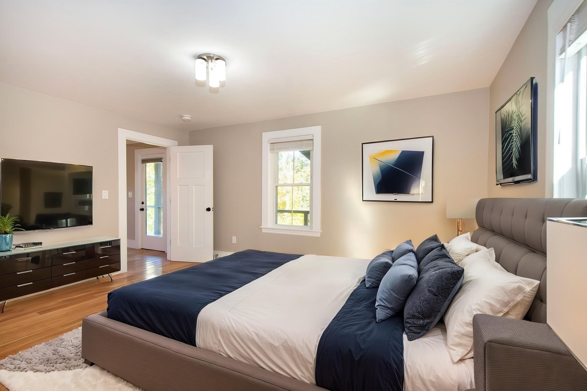 Furnished bedroom with a large navy-and-white bed, hardwood floors, and a wall-mounted television.