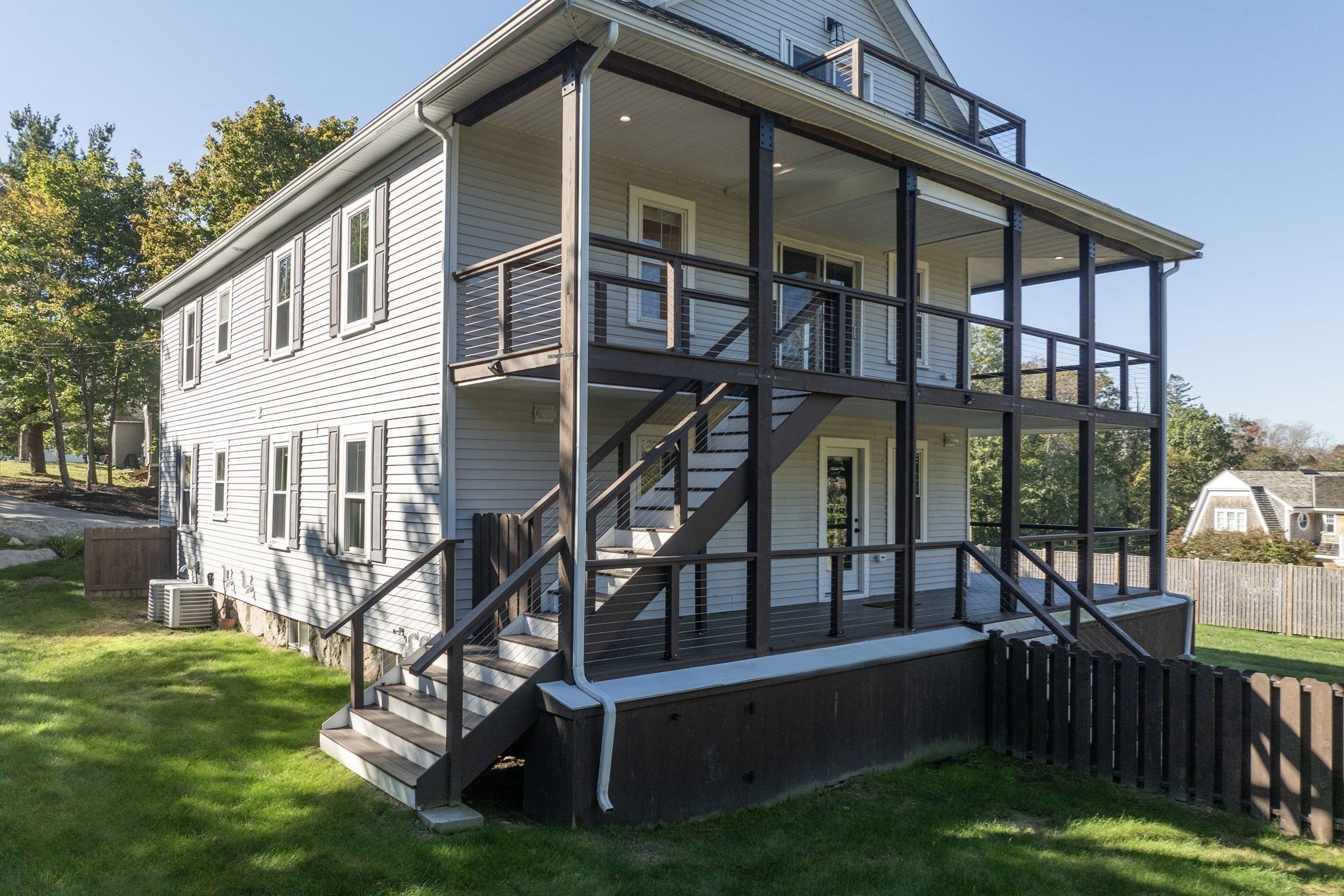 Home’s rear exterior with a large covered deck, dark railings, and stairs to the lawn.