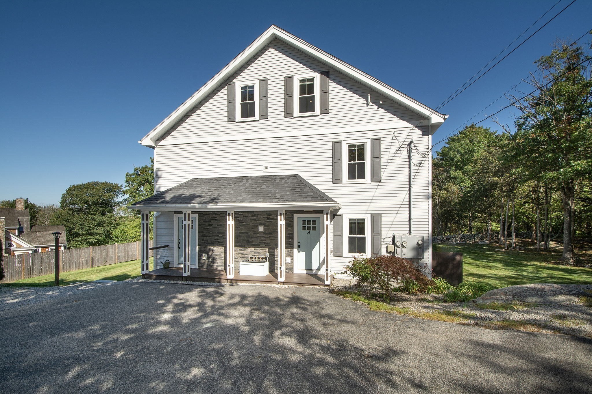 White two-story house with gray shutters and a covered stone-backed porch.
