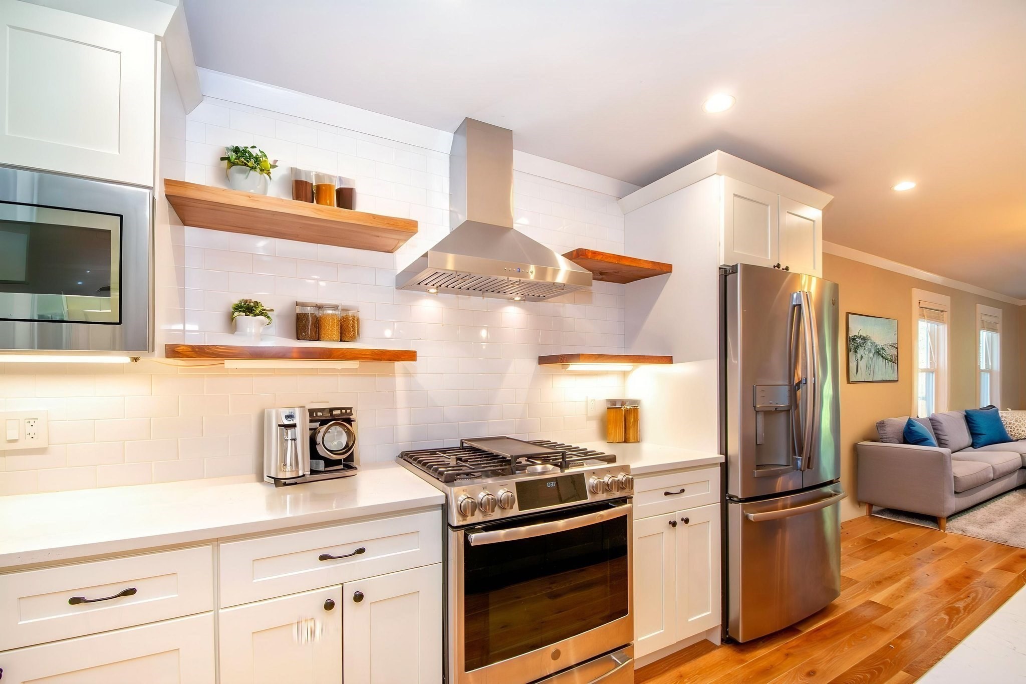 Kitchen with white shaker cabinets, wood shelves, stainless steel appliances, and adjoining living room.