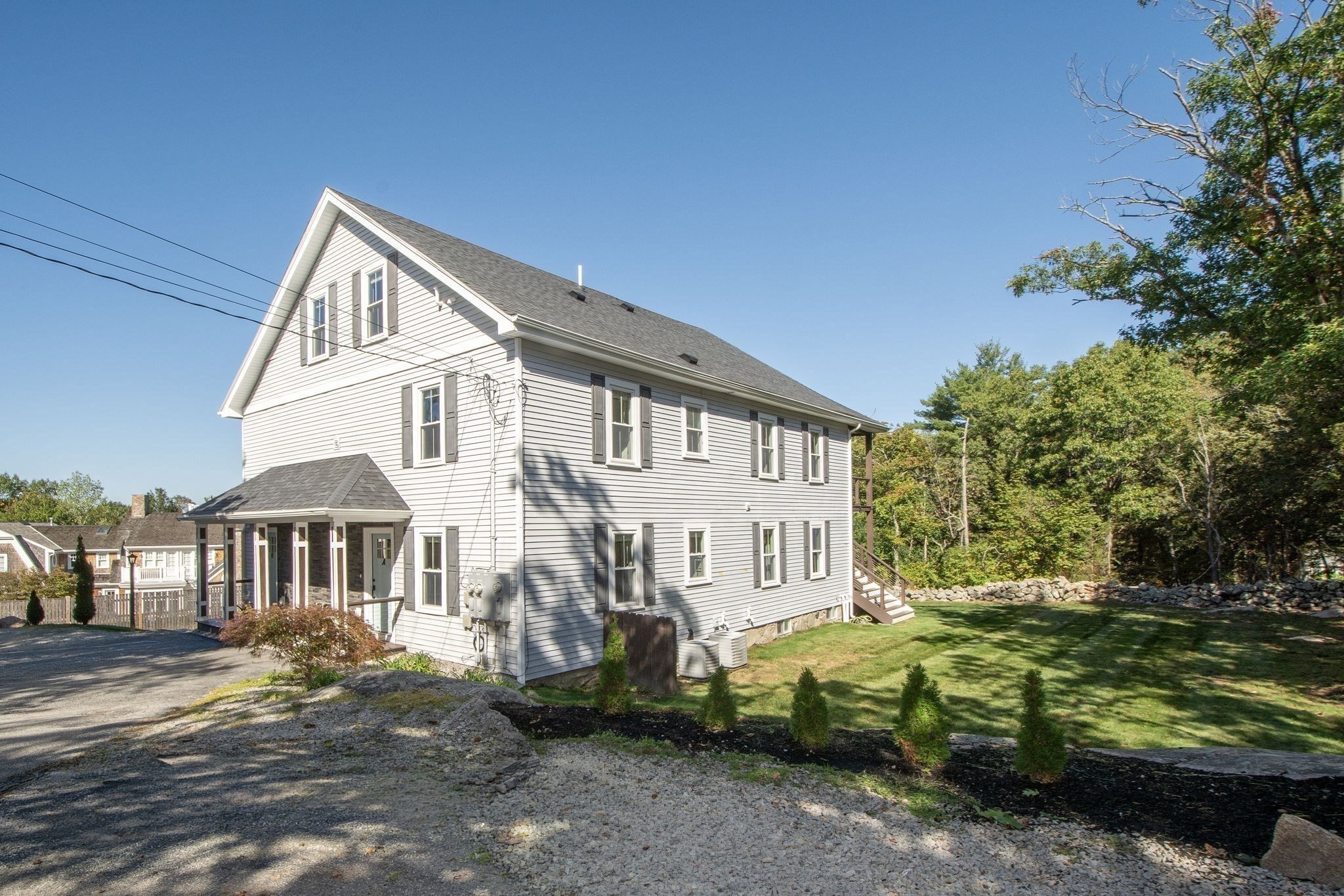 White two-story house with a steep gabled roof, covered entry, and landscaped lawn.
