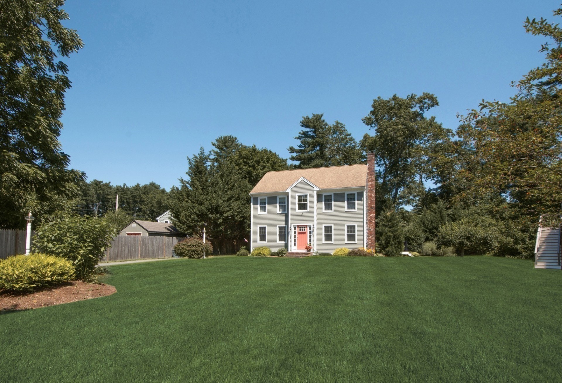 Two-story gray house with a red front door and brick chimney, set behind a broad lawn.