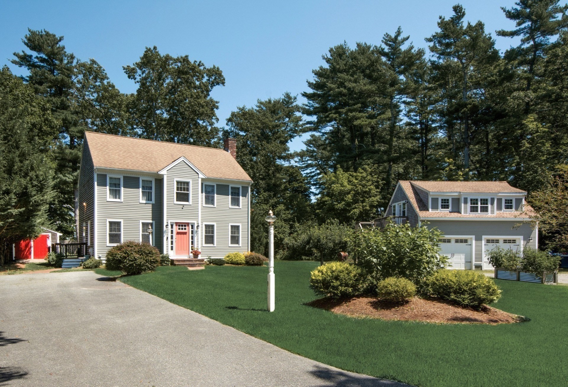 Gray two-story home with a coral front door, detached garage, and landscaped lawn.