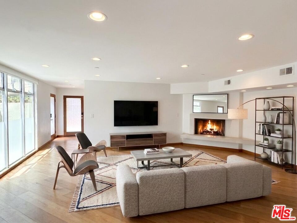Staged living room with a lit fireplace, wall-mounted TV, and sliding glass doors.