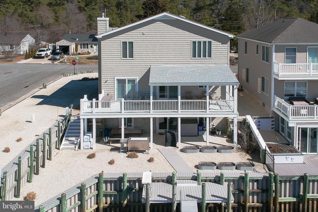 Raised two-story coastal home with white-railed decks, exterior stairs, and a gravel yard.