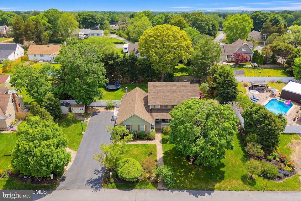 Aerial view of a house with a broad driveway, mature trees, and a landscaped front lawn.