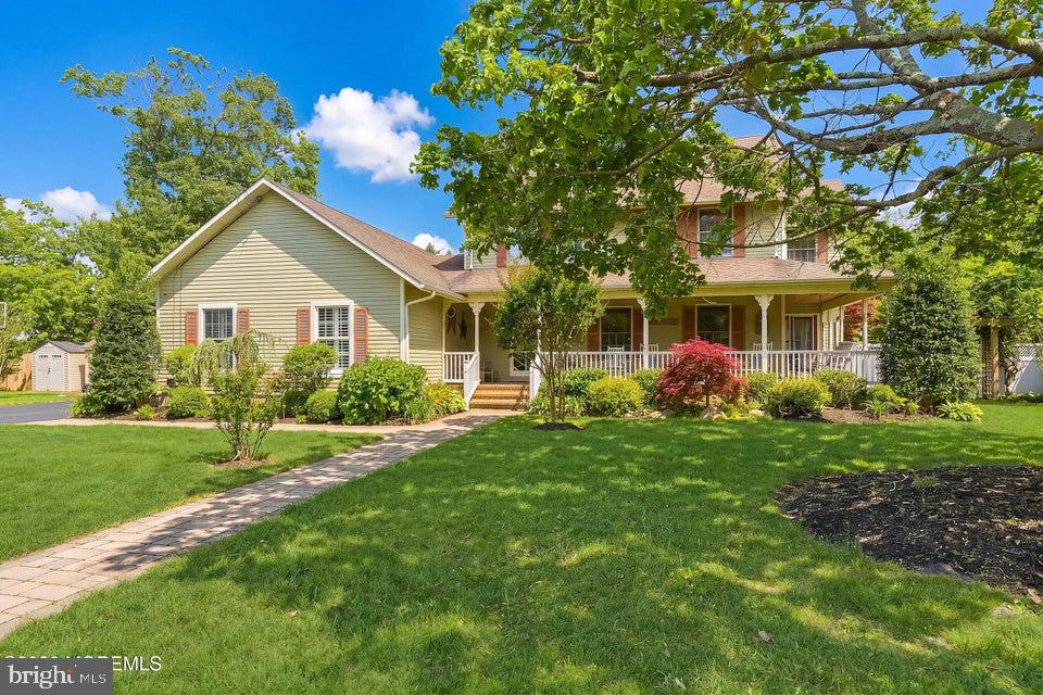 Two-story pale yellow house with a covered porch, landscaped garden, and stone walkway across the lawn.