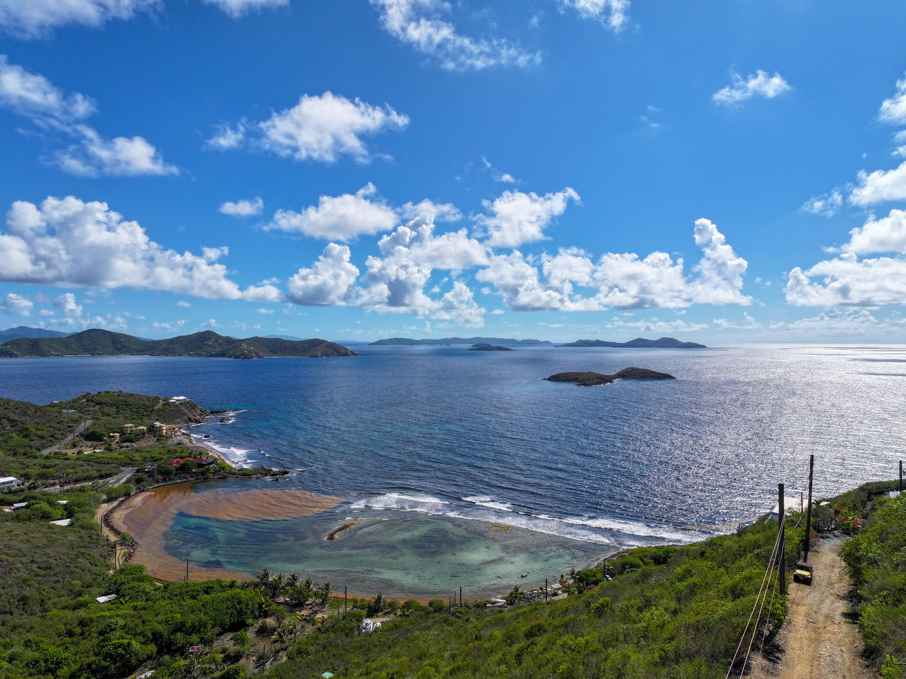 Caribbean bay with turquoise shallows, green hills, and small islands beneath a cloud-filled sky.