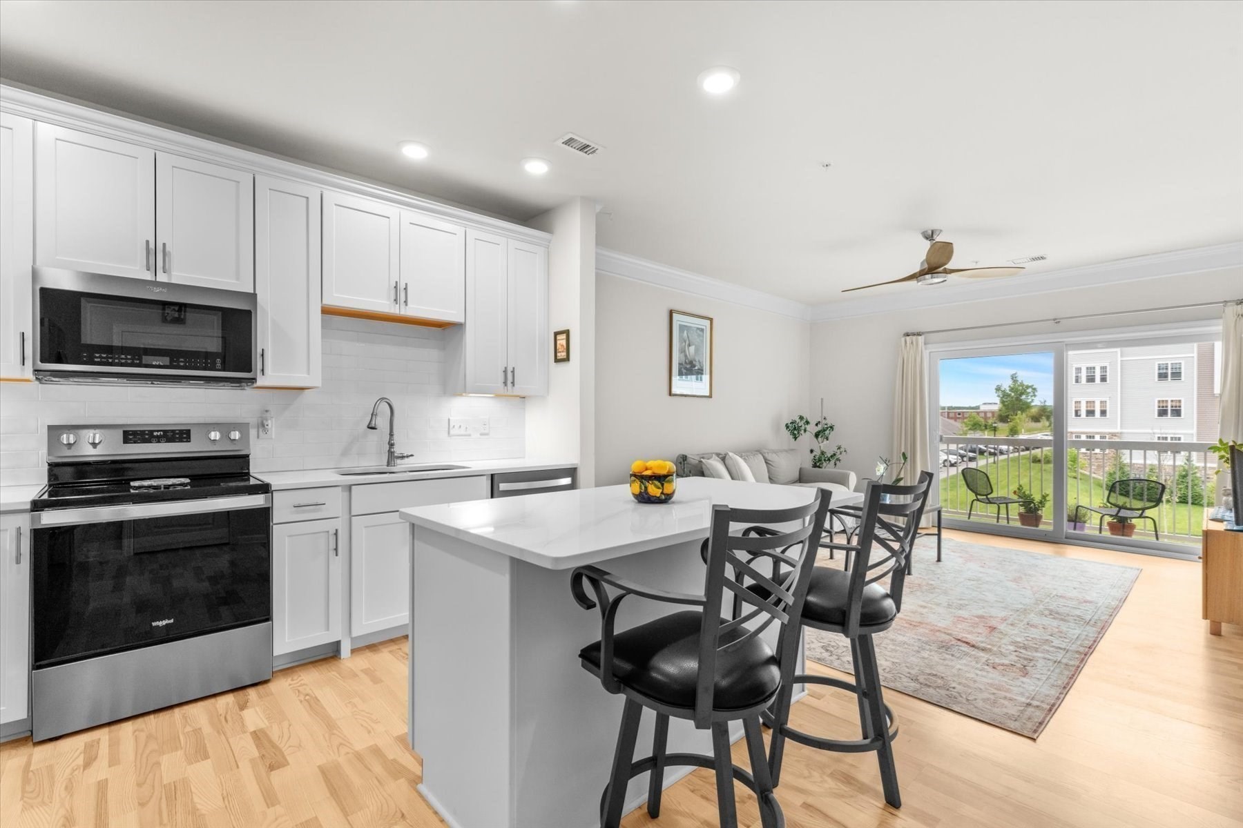 Kitchen and dining area with a white island, stainless steel appliances, and sliding doors to a balcony.