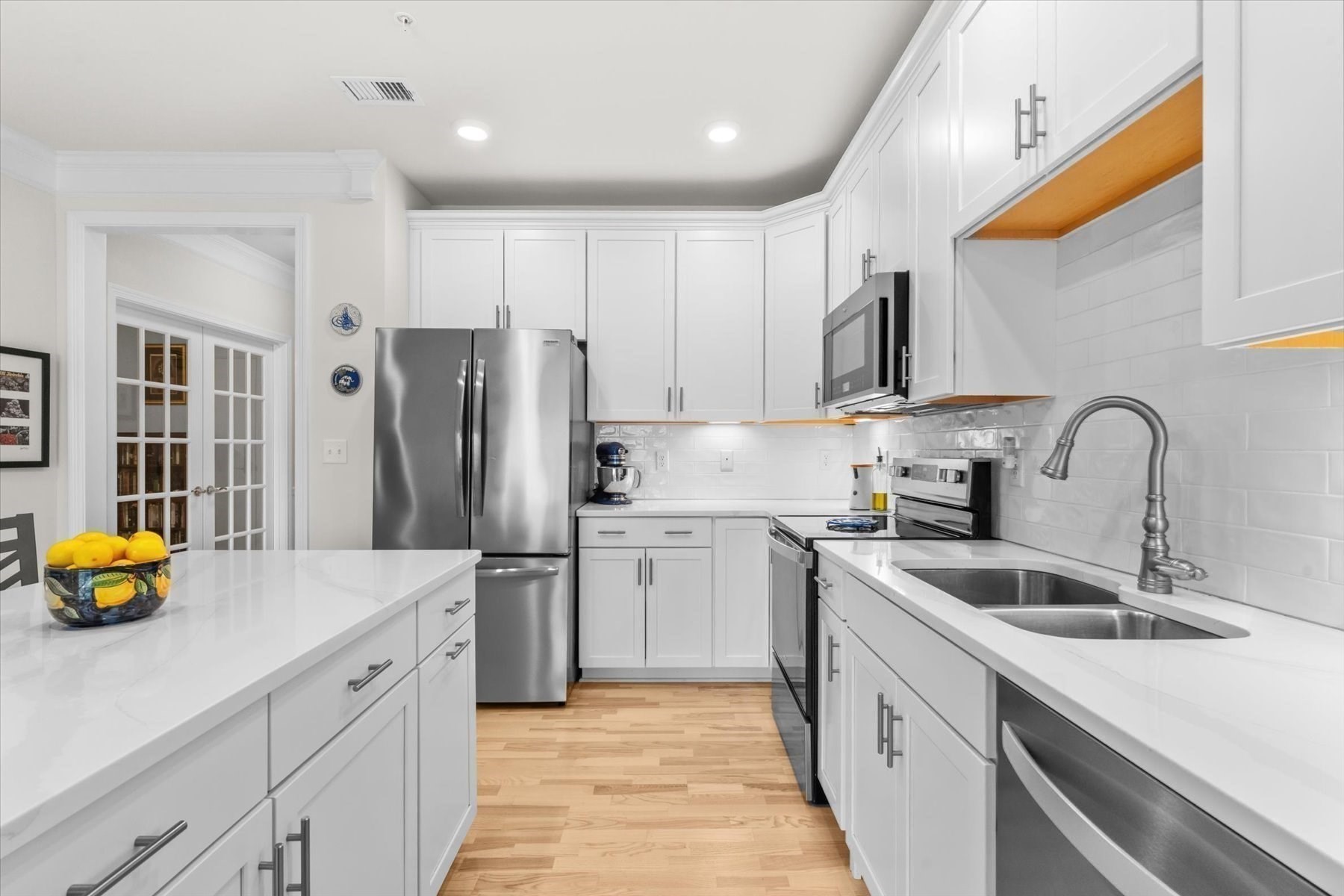 Bright white kitchen with a large island, stainless steel appliances, and light wood floors.