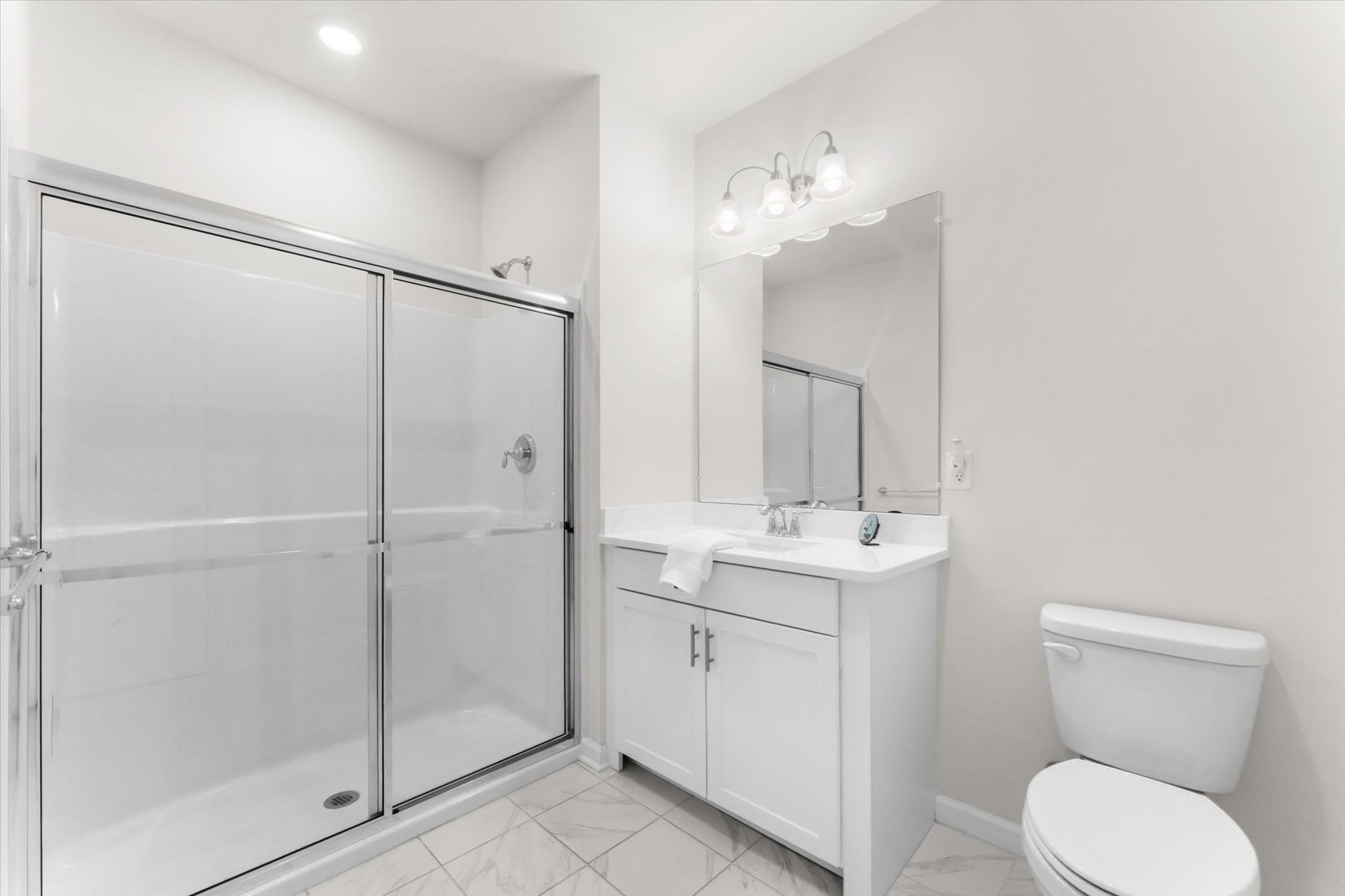 Bathroom with a glass-enclosed shower, white vanity, large mirror, and marble-look tile floor.