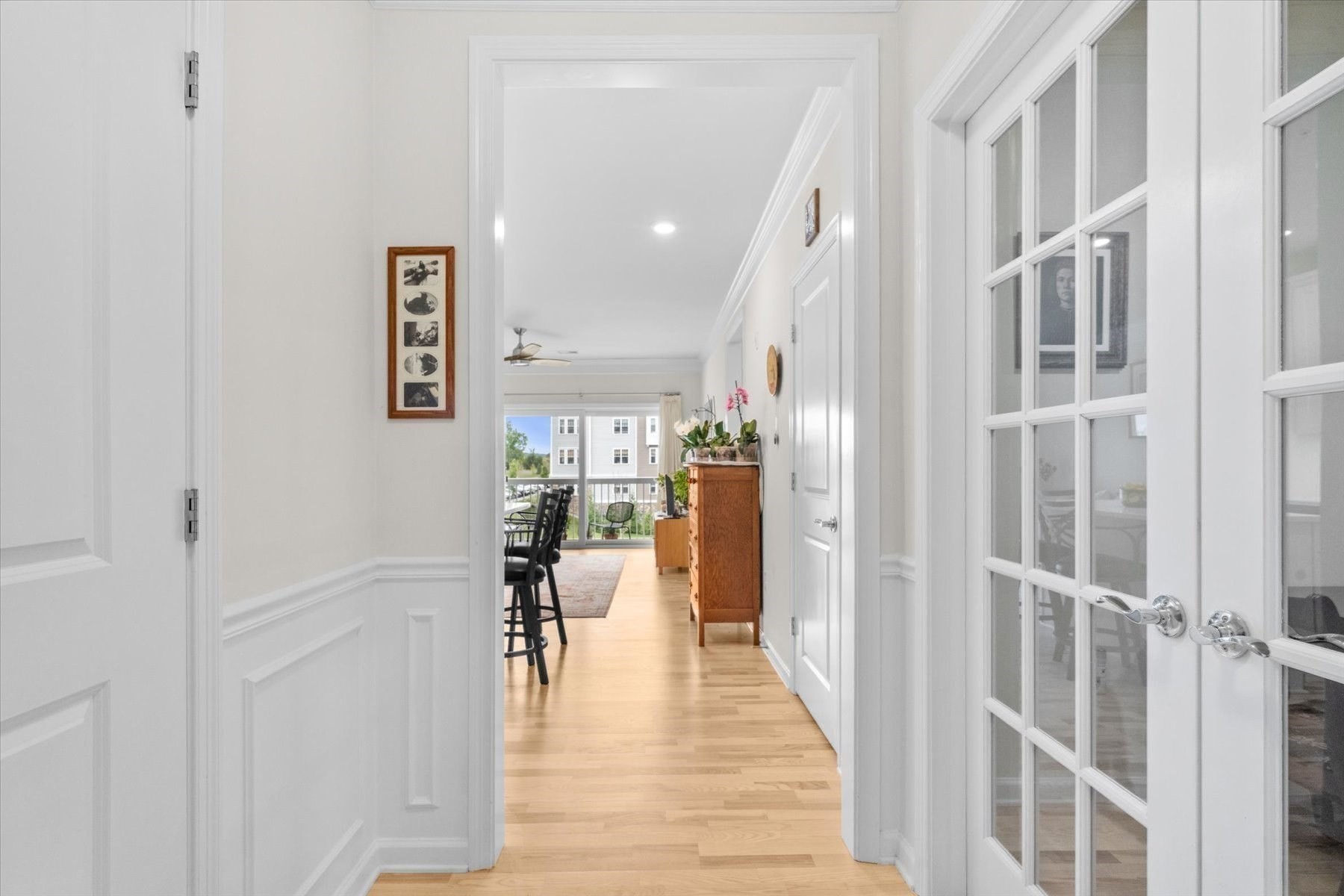 Apartment hallway with hardwood floors and French doors, leading to a dining area and balcony.