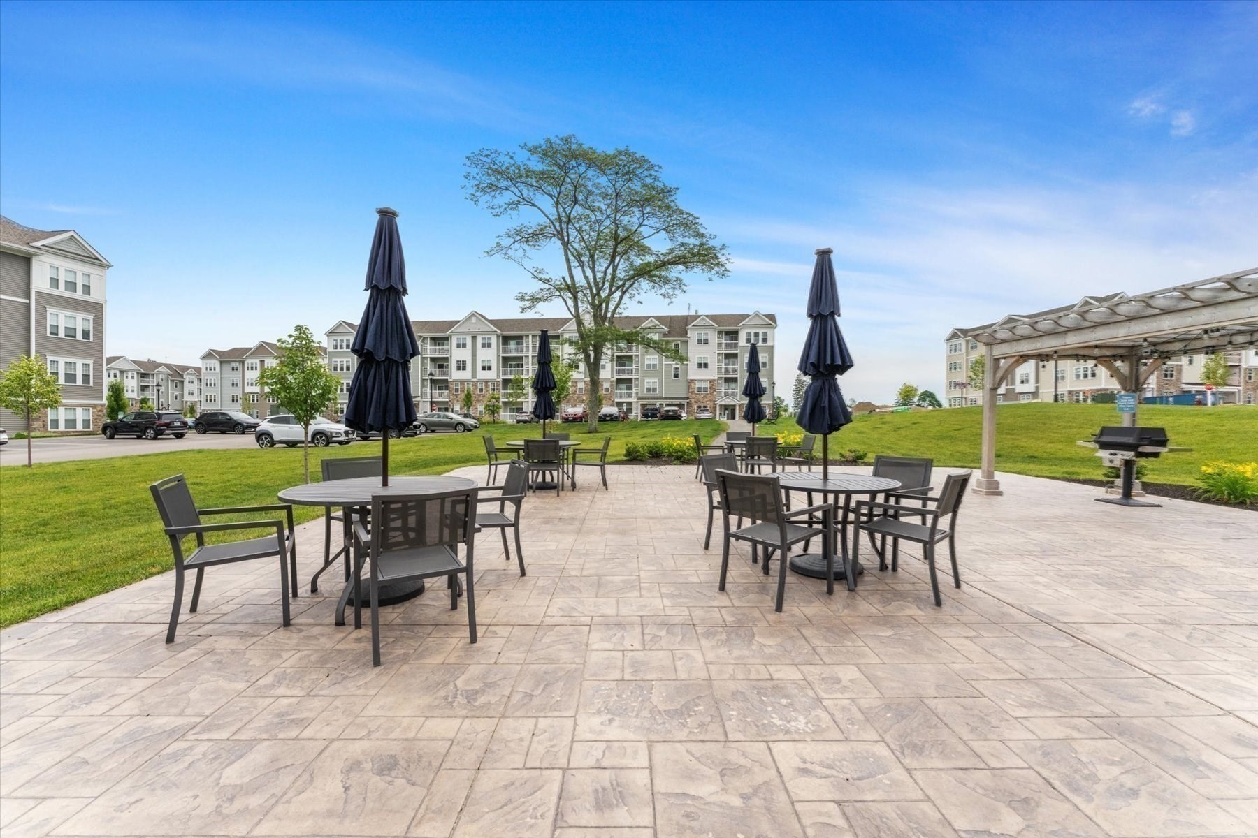 Apartment community patio with stone paving, outdoor dining tables, closed umbrellas, and a pergola.
