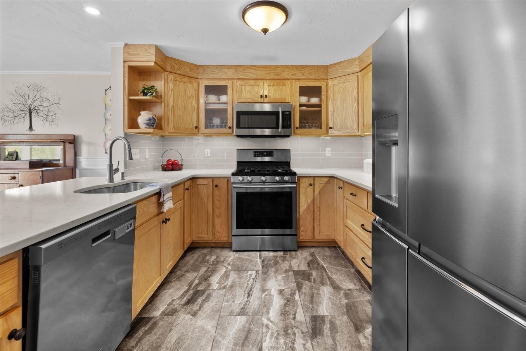 Kitchen with honey-colored wood cabinets, stainless steel appliances, and stone-pattern tile flooring.