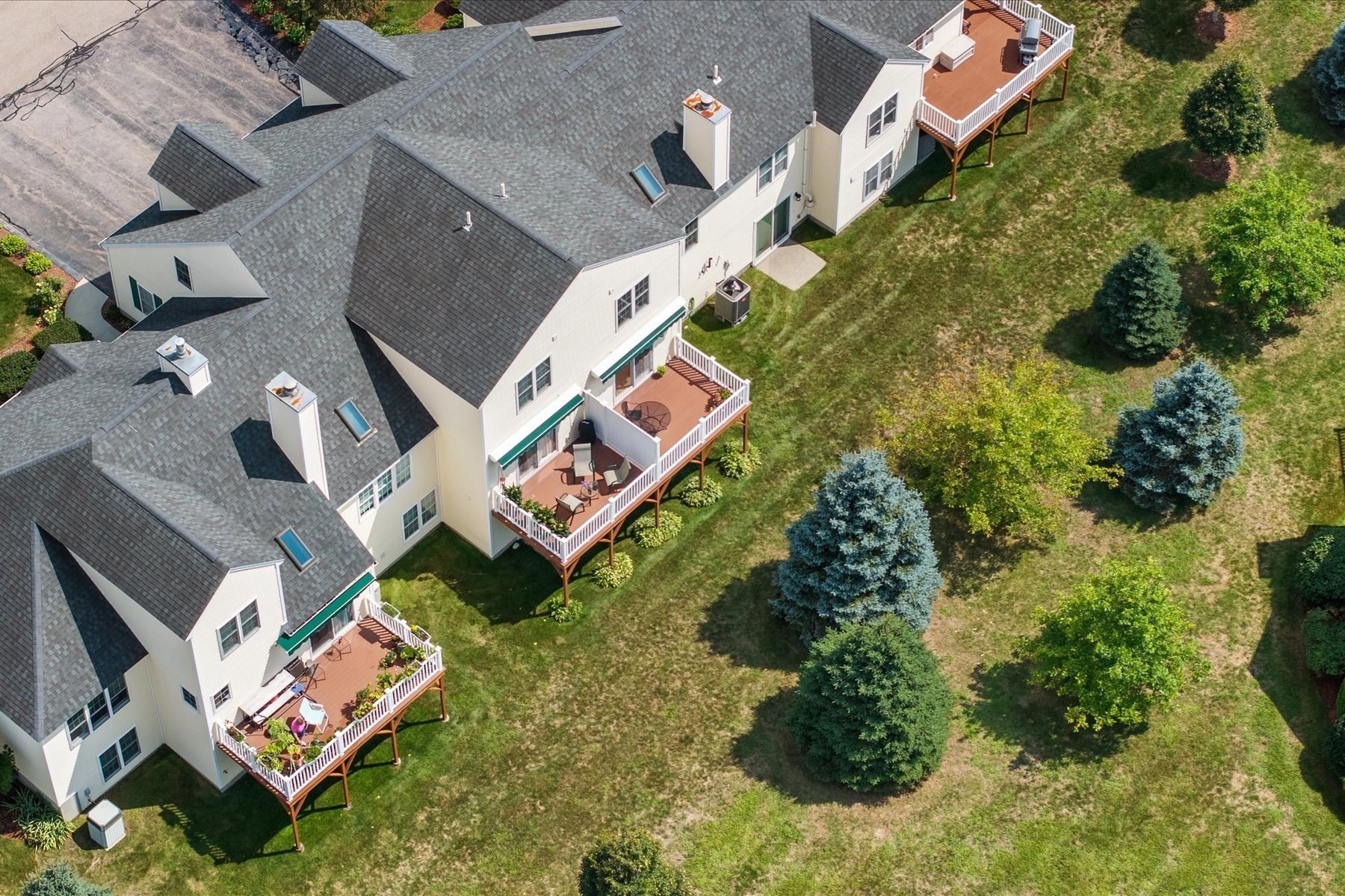 Aerial view of attached homes with raised wooden decks beside a tree-dotted lawn.