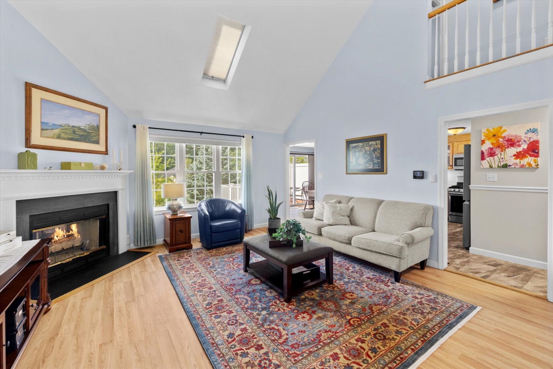 Living room with a vaulted ceiling, fireplace, large windows, and patterned rug.