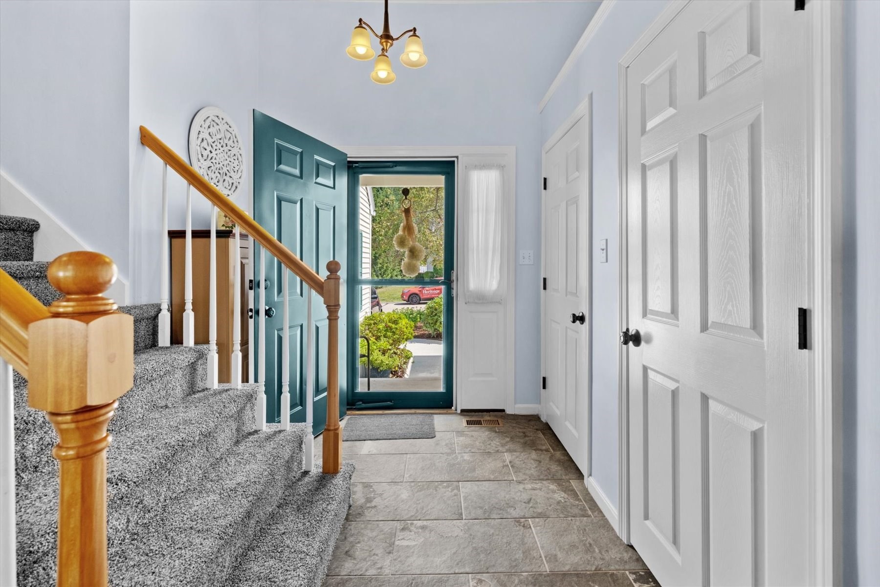 Entry foyer with carpeted staircase, teal front door, and gray tile flooring.