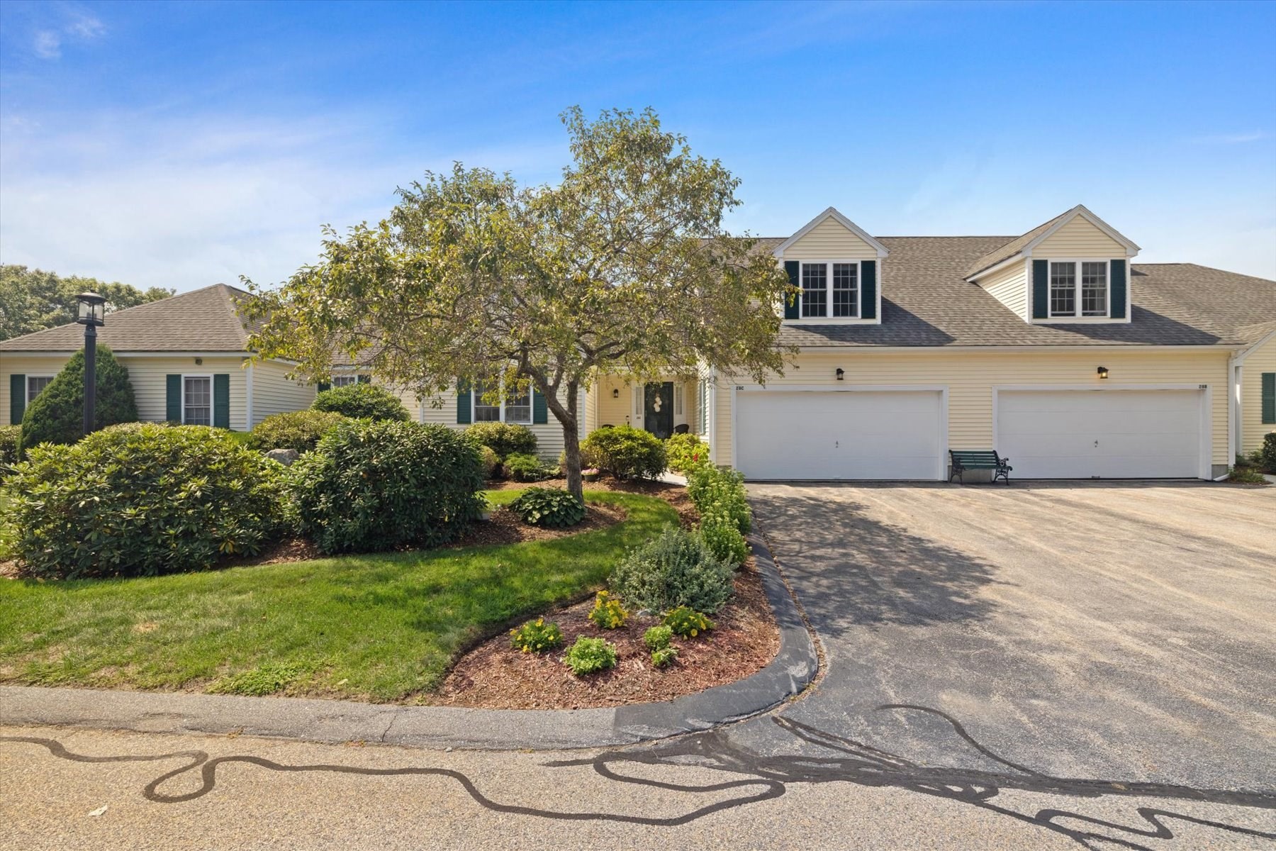 Cream-colored home with two garage doors, dormer windows, and a landscaped front yard.