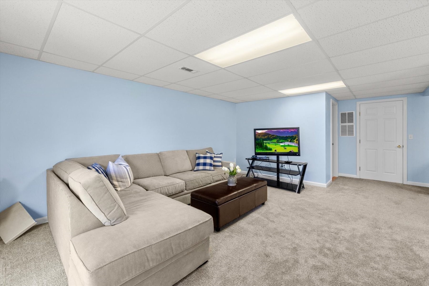 Furnished living room with a beige sectional, brown ottoman, blue walls, and television.