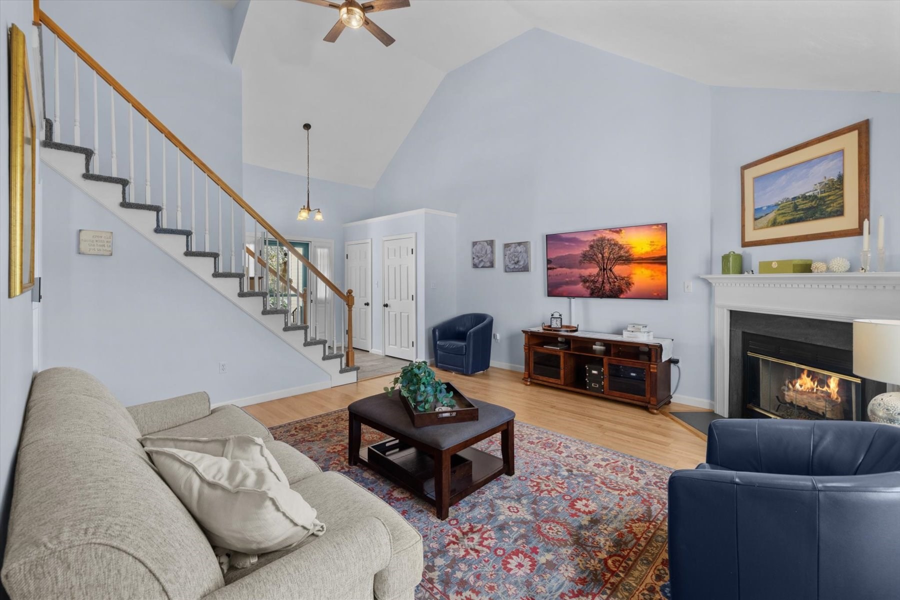 Living room with a vaulted ceiling, staircase, fireplace, and seating around a patterned rug.