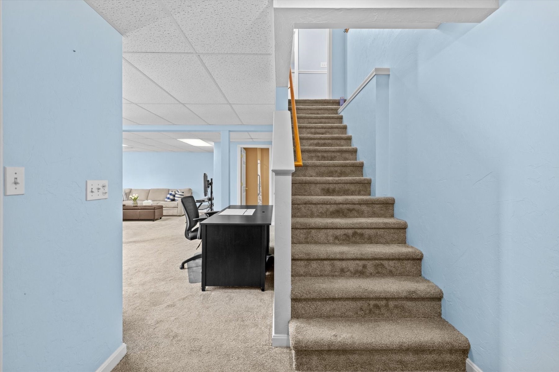 Carpeted staircase beside a home office and sitting area with light blue walls.