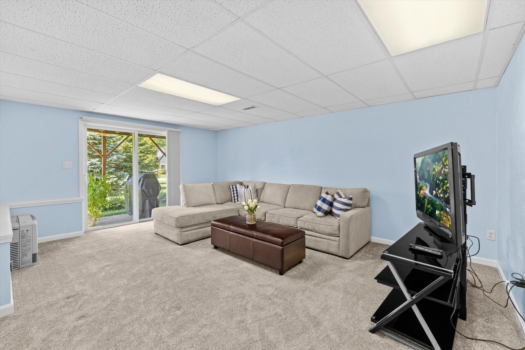 Living room with a large sectional sofa, beige carpet, and sliding glass door to a green yard.