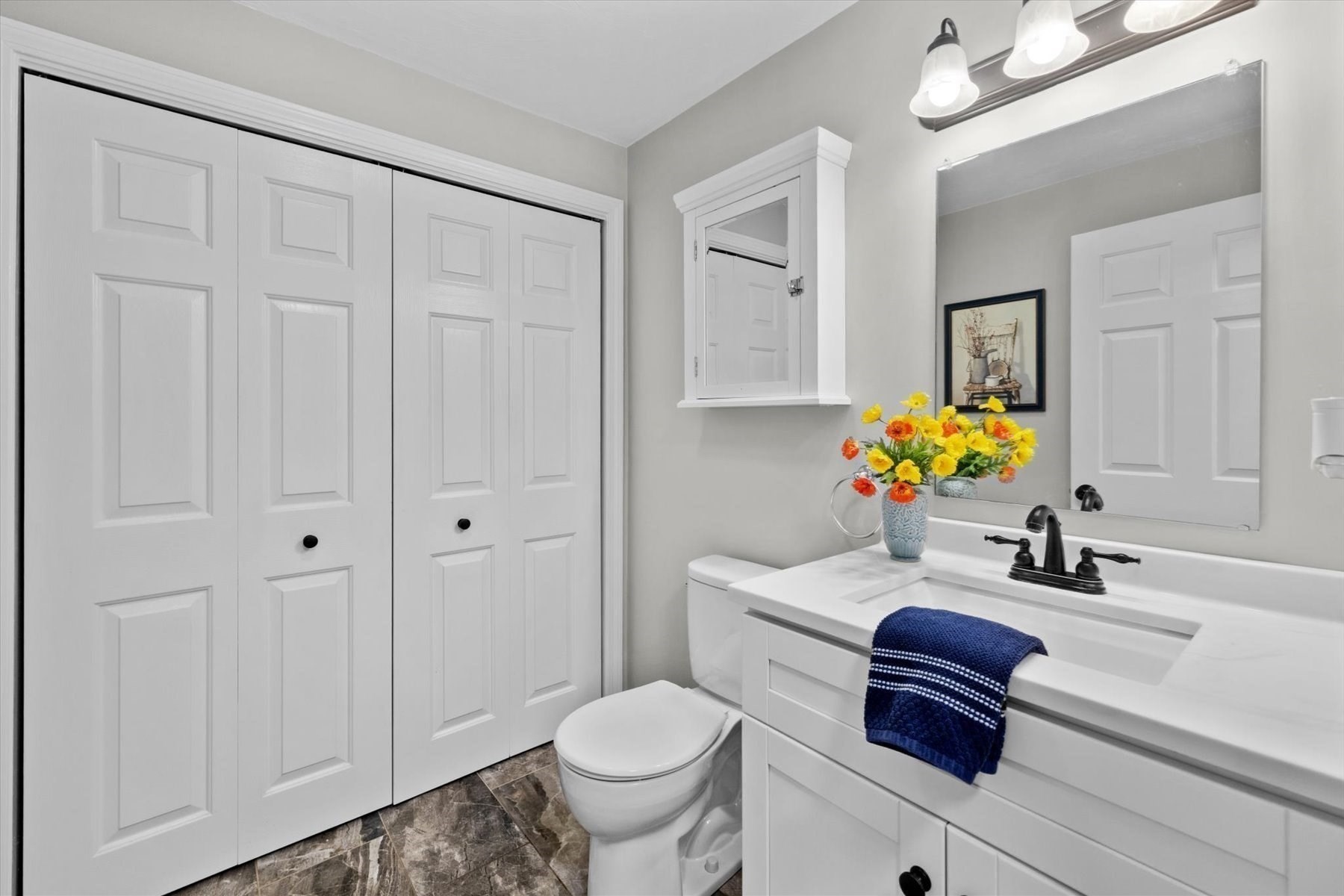 Bathroom with white vanity, black faucet, mirrored wall, and colorful flowers on the counter.