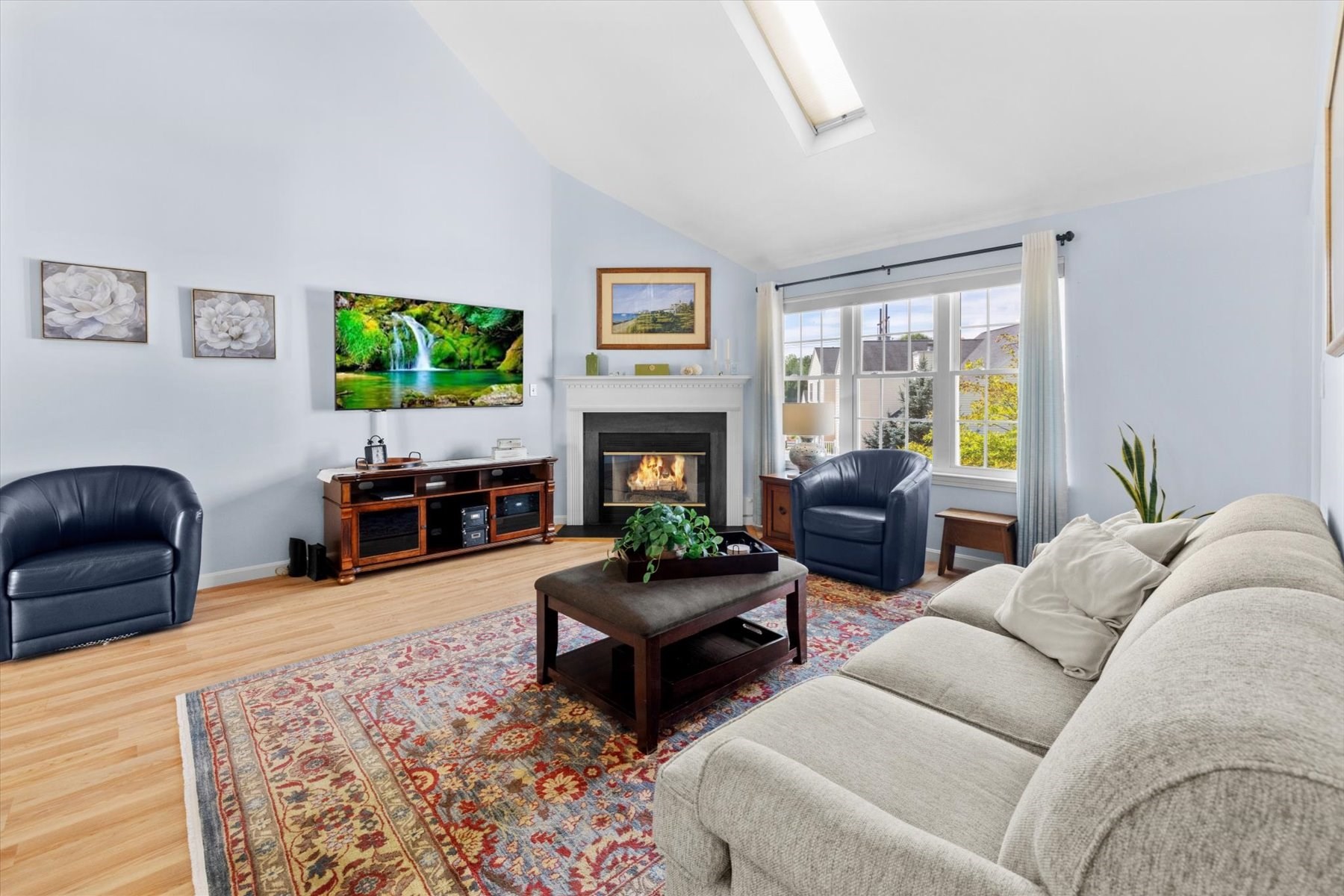 Living room with a fireplace, large windows, patterned rug, and gray sectional sofa.