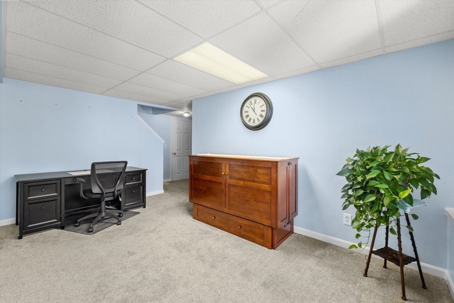 Furnished office with a black desk, wooden cabinet, and potted plant.