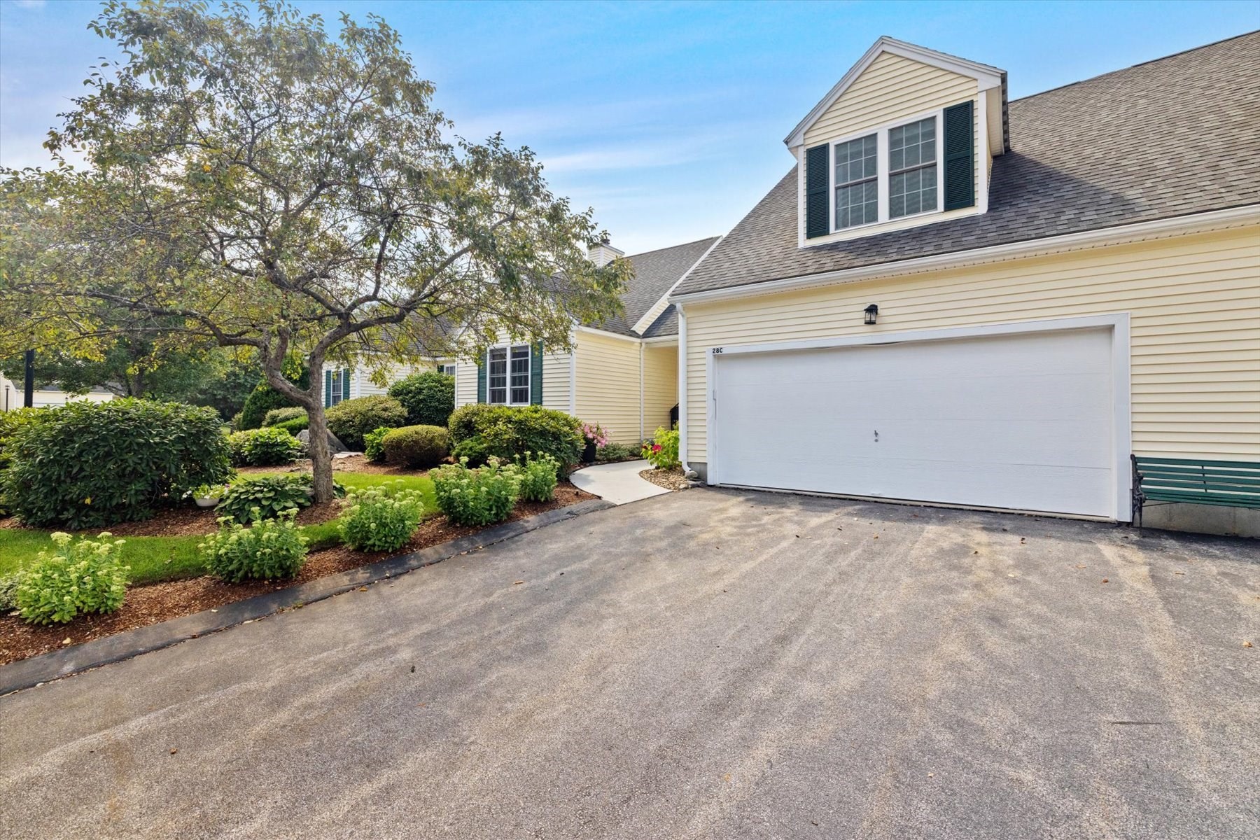 Pale yellow home with a large white garage, landscaped garden, and mature tree.
