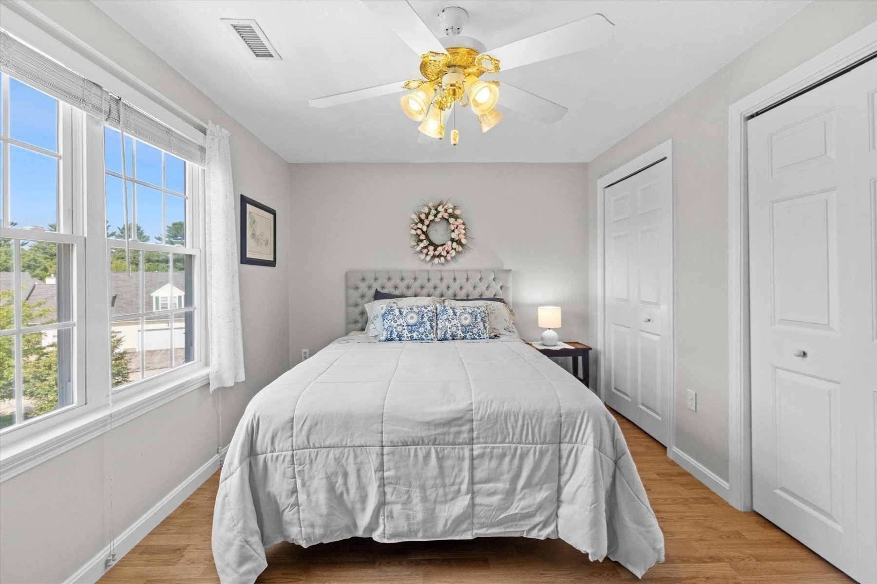 Furnished bedroom with a large bed, wide windows, hardwood floors, and a ceiling fan.