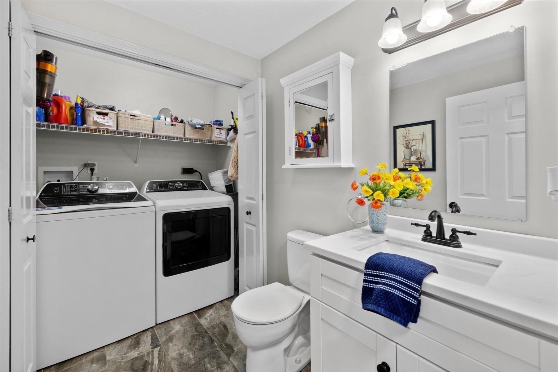 Bathroom with white vanity and toilet beside a laundry closet with washer and dryer.