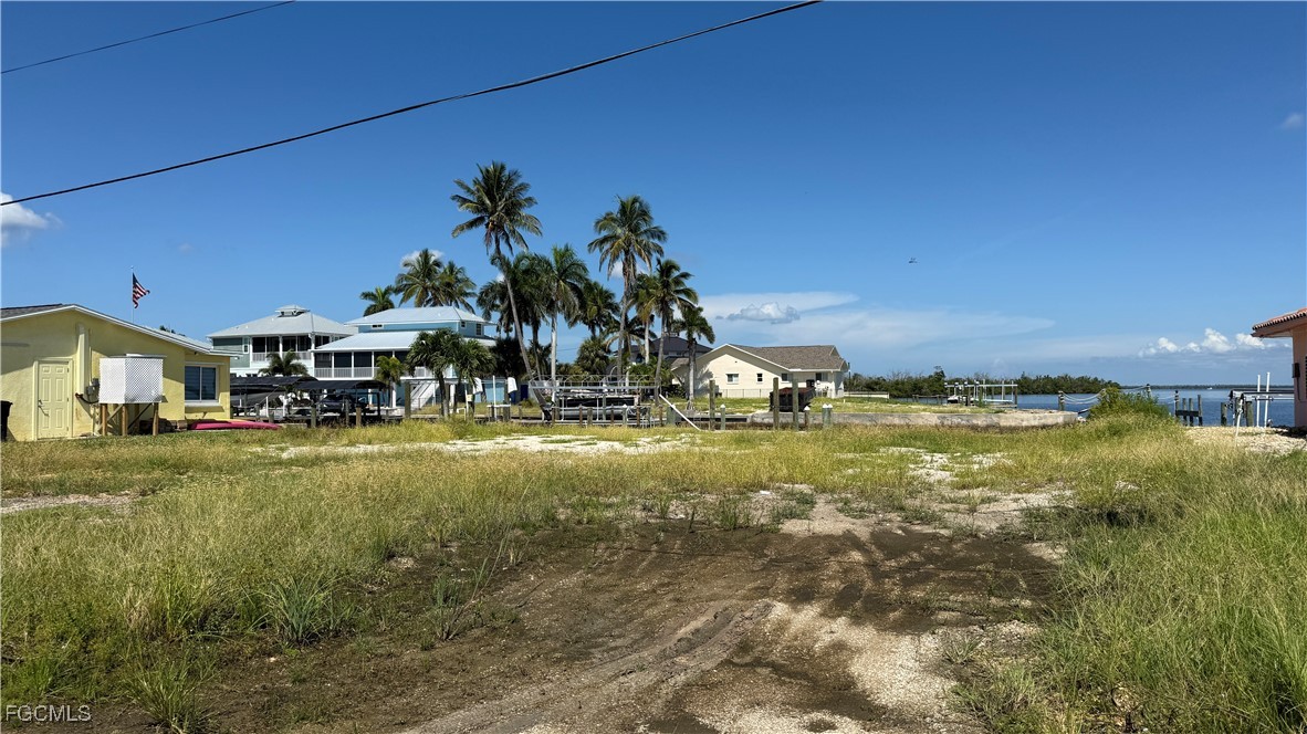 Vacant grassy lot beside a canal, with neighboring homes and palm trees.