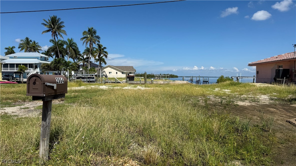 Vacant grassy waterfront lot with a canal, docks, palm trees, and mailbox marked 2864.