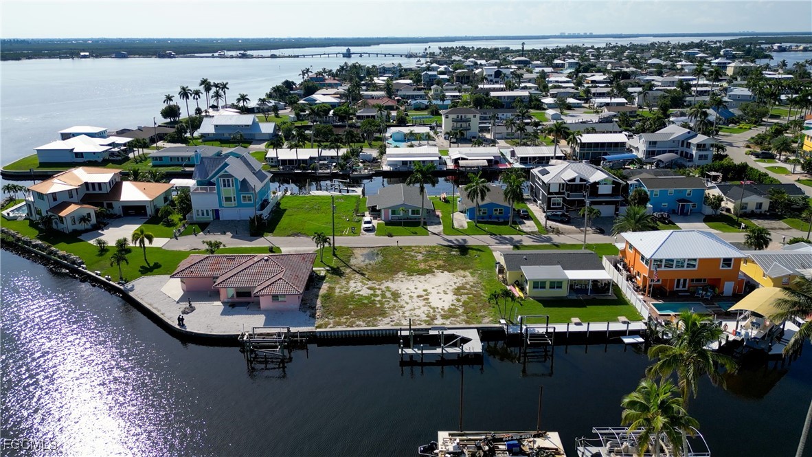 Vacant waterfront lot beside a canal, with neighboring homes, docks, and a bridge in the distance.