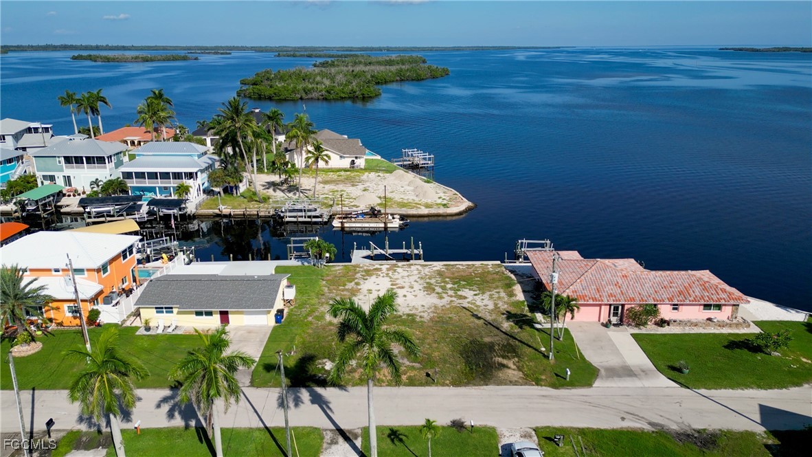 Vacant waterfront lot beside neighboring homes, with docks, palms, and a mangrove island across the water.