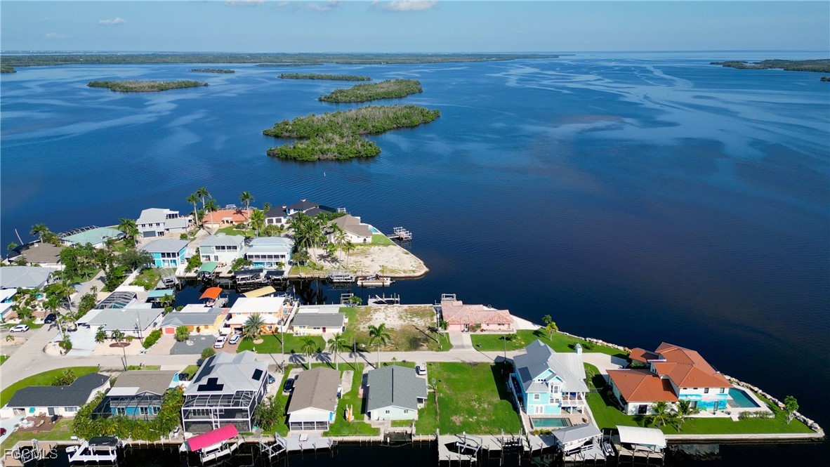 Aerial view of waterfront homes and docks beside a broad bay dotted with mangrove islands.