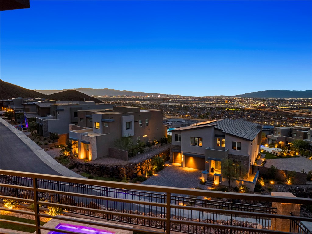 Modern hillside homes overlook a valley of city lights and distant mountains at dusk.