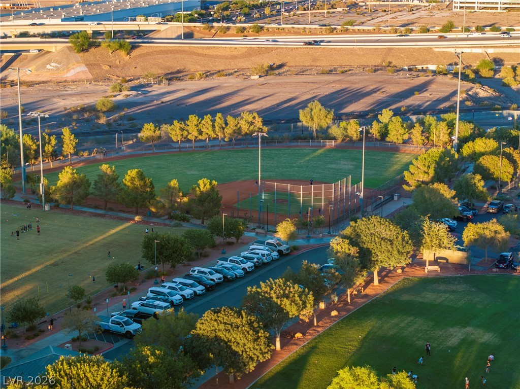 Aerial view of a baseball field and neighboring sports fields, with parking and a highway beyond.