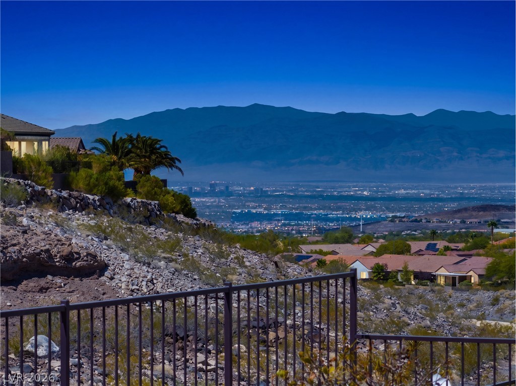 Valley and mountain view at dusk from a rocky hillside, with homes below and a railing in the foreground.