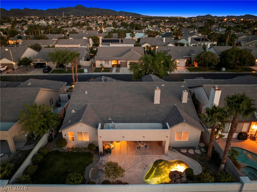 Aerial view of a home’s backyard with a swimming pool and covered patio at dusk, with mountains beyond the neighborhood.