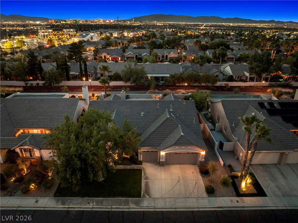 Aerial view of a Las Vegas home at dusk, with city lights and mountains beyond the neighborhood.