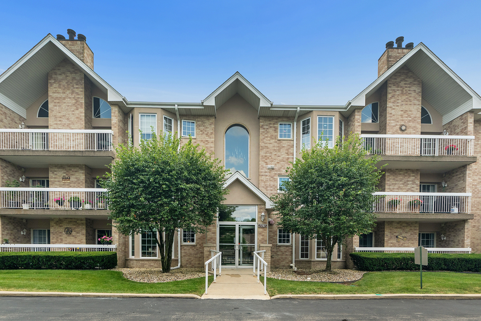 Brick condominium building with white balconies, peaked roofs, and a central glass entrance.
