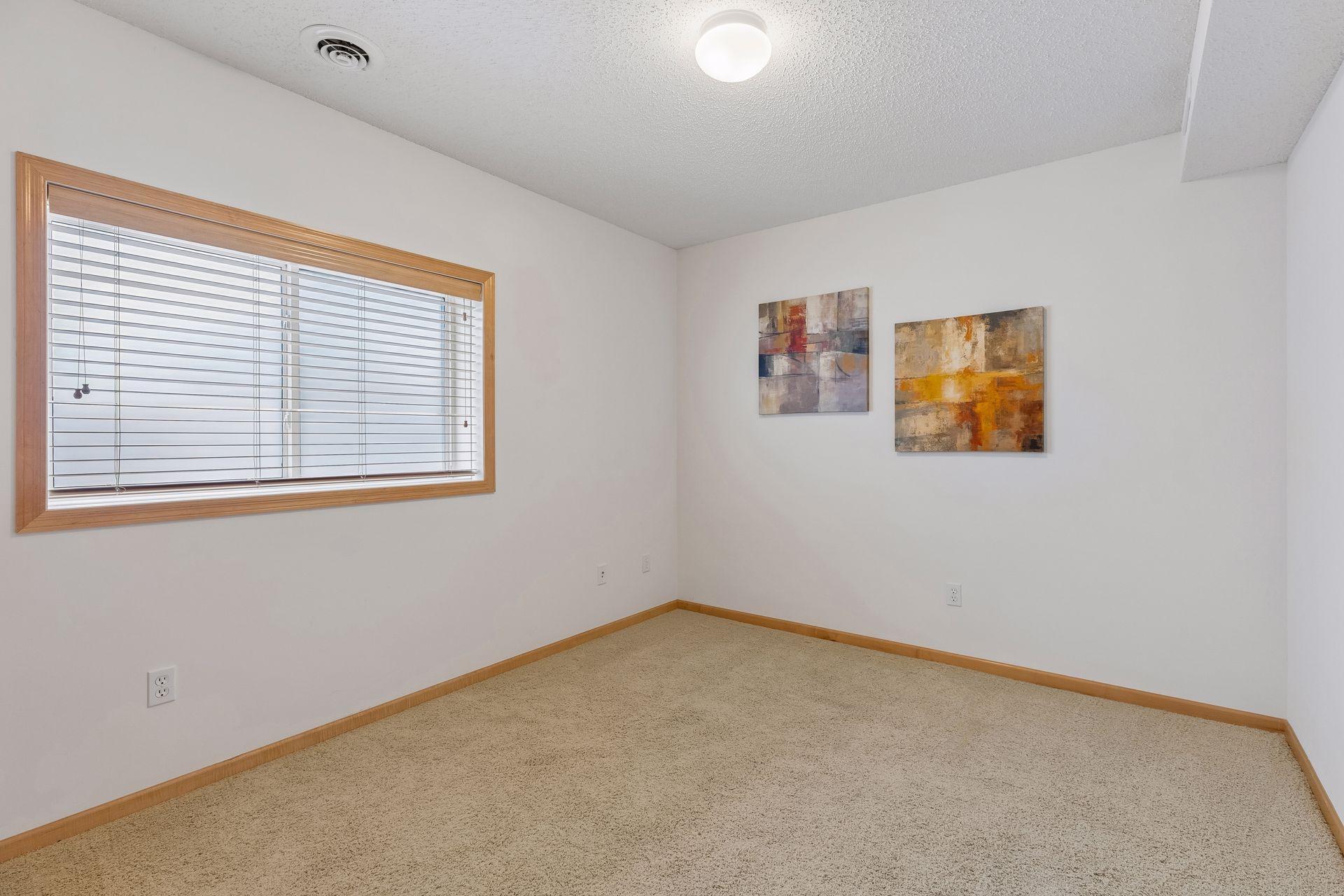 Carpeted room with a wide wood-trimmed window and two abstract paintings.