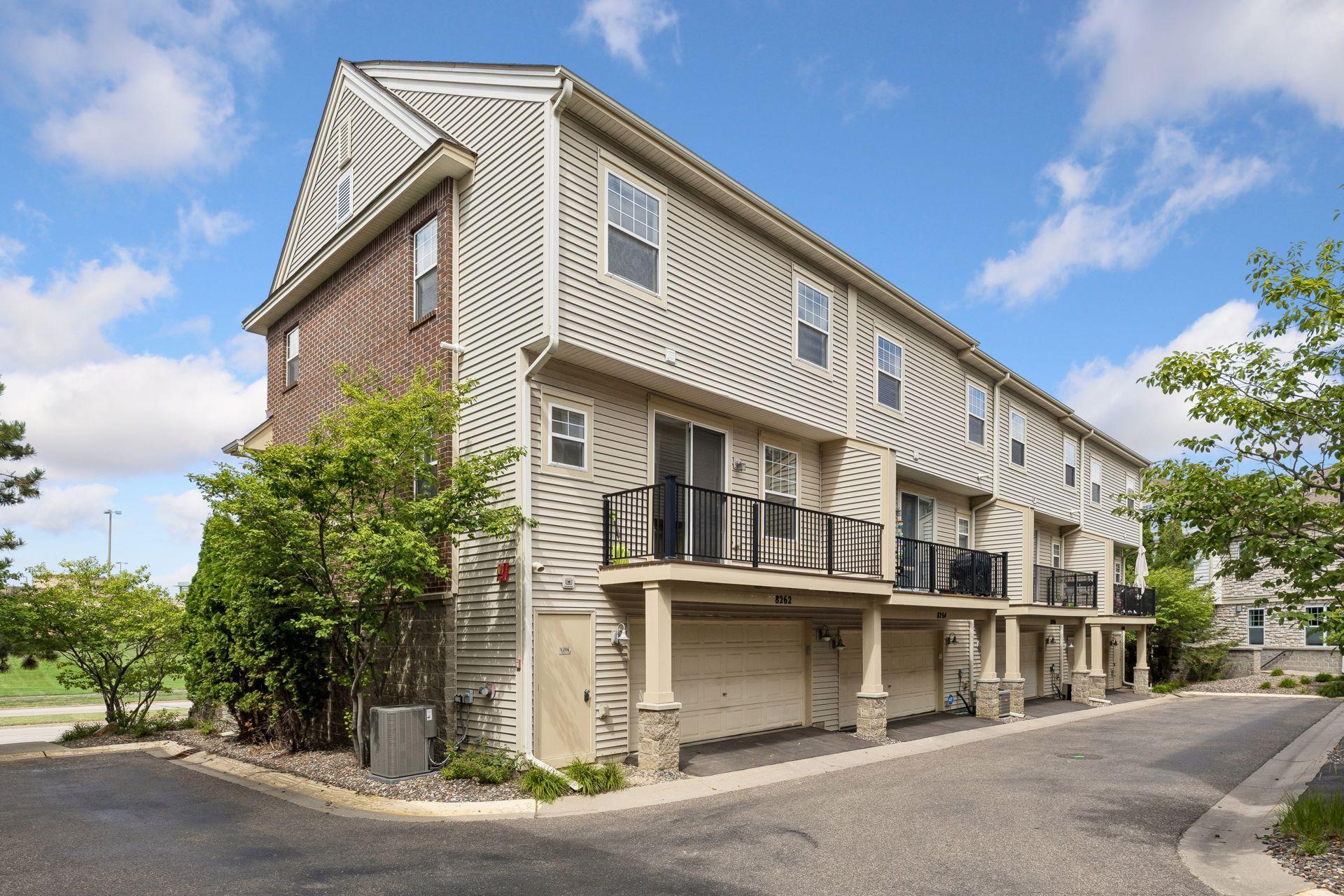 Townhouse exterior with beige siding, brick accents, upper-level balconies, and attached garages.
