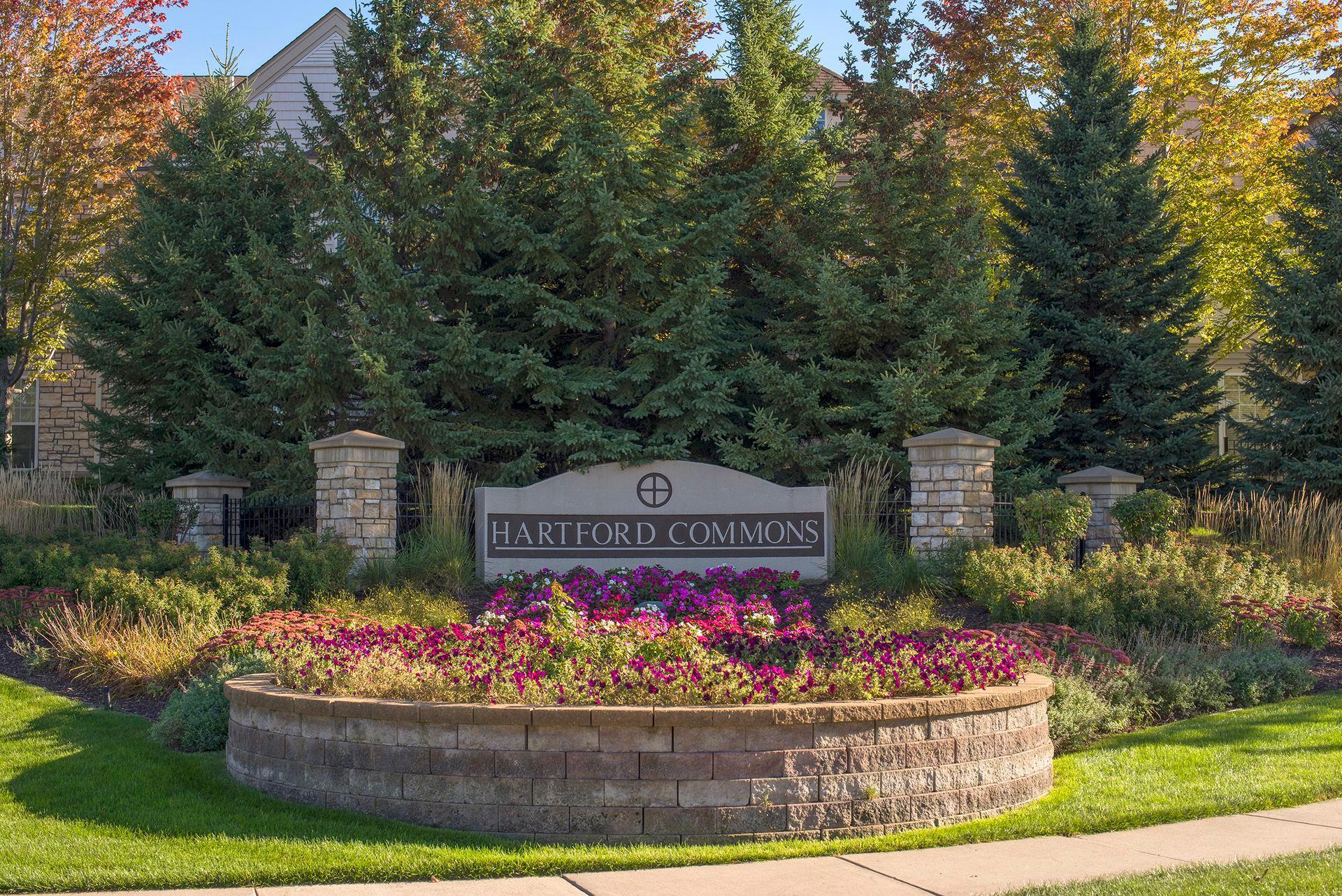 Hartford Commons entrance sign among stone pillars and a colorful flower bed.